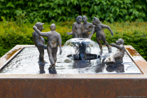 Bronze, Cortenstahl. Skulpturen versammelt um einen Brunnen.
